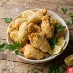 Fiori di zucca in pastella dorati e croccanti serviti in una ciotola di ceramica con spicchi di limone e prezzemolo fresco.